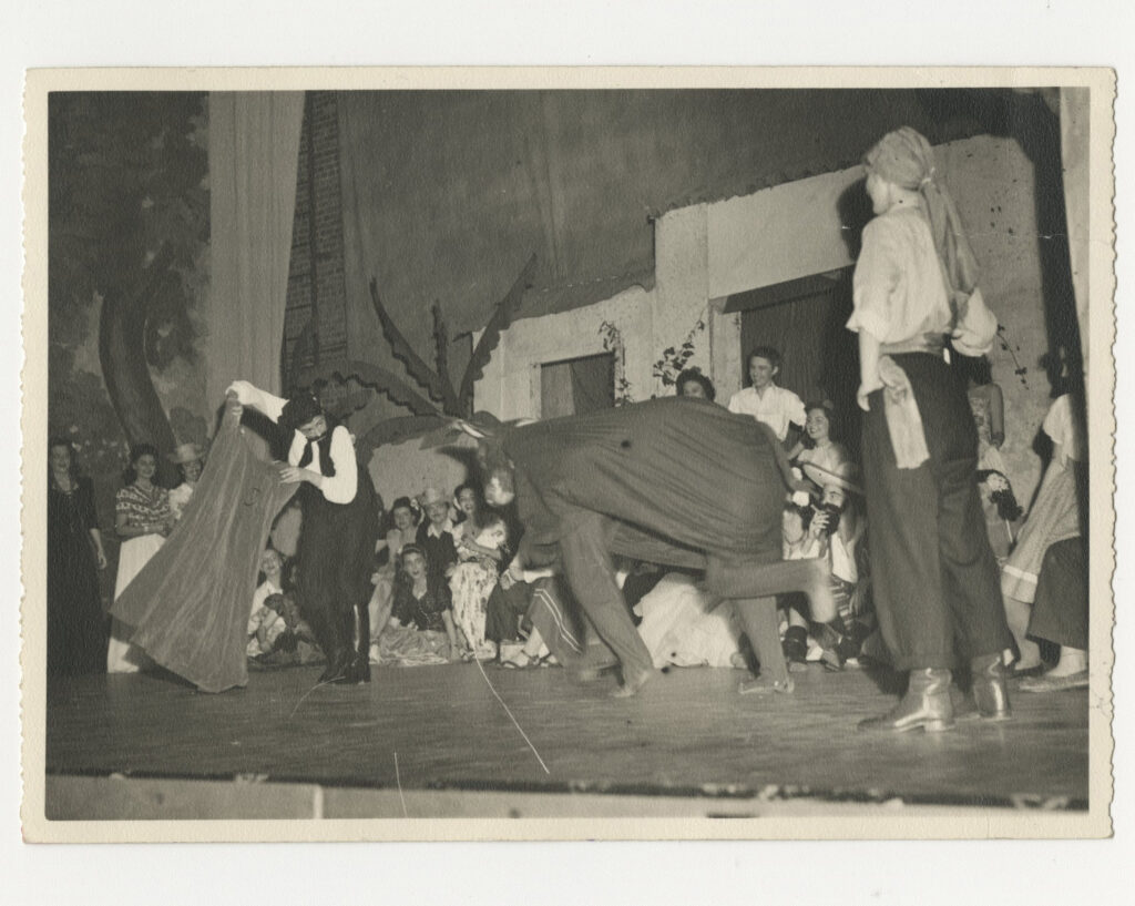 Students on a stage, demonstrating bull fighting with a person as the bull.